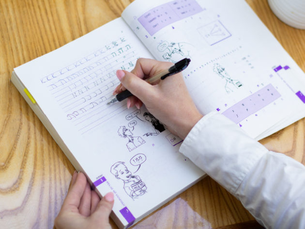 Student writing in Hebrew in their textbook.