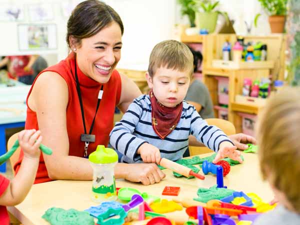 Laughing preschool teacher helps child with blocks