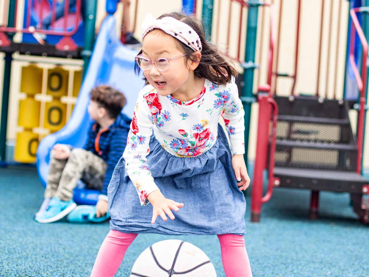 Preschool girl dribbles basketball on playground