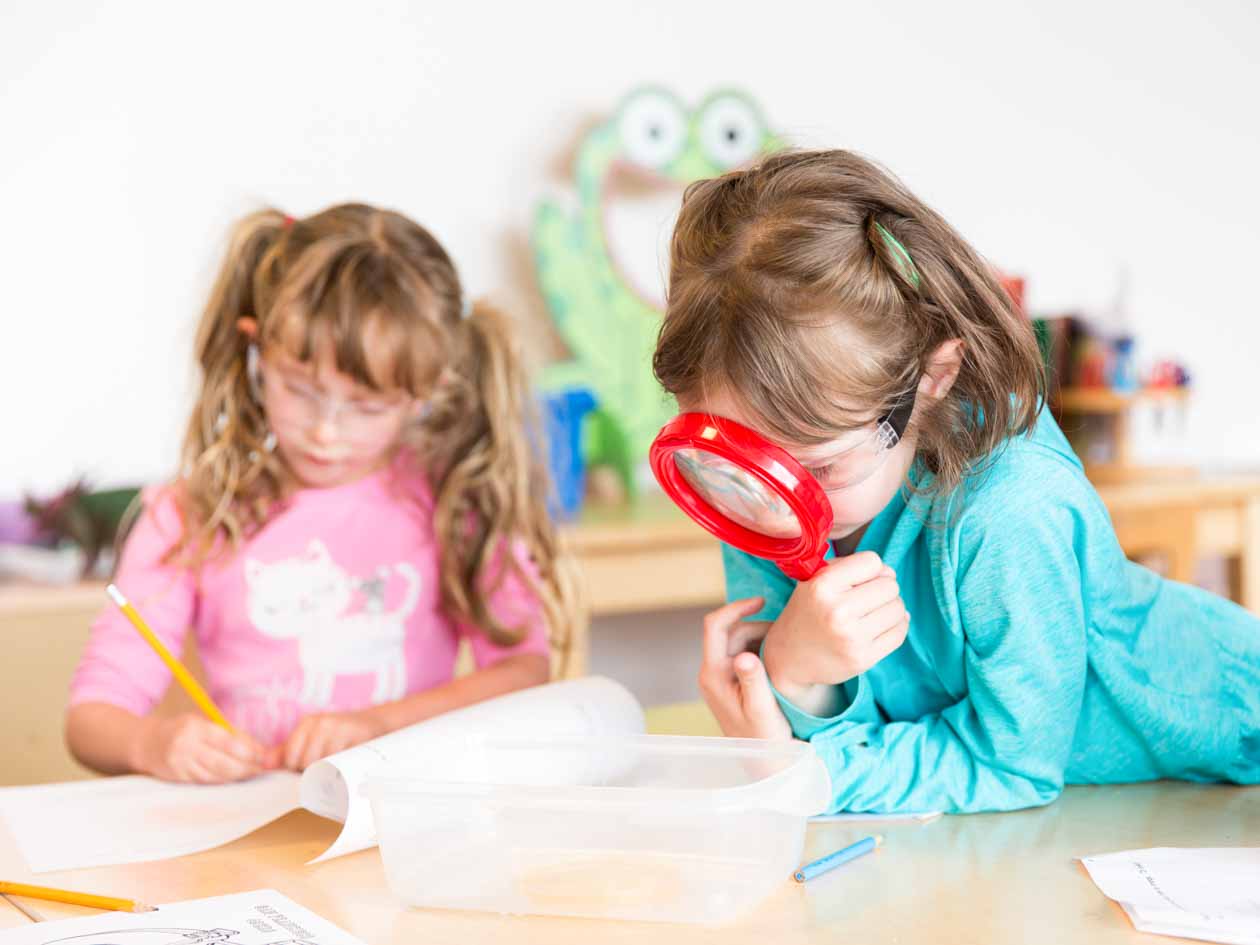 Preschool girl uses large red magnifying glass