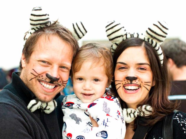 Parents with cat whisker face paint hold young child during Purim celebration