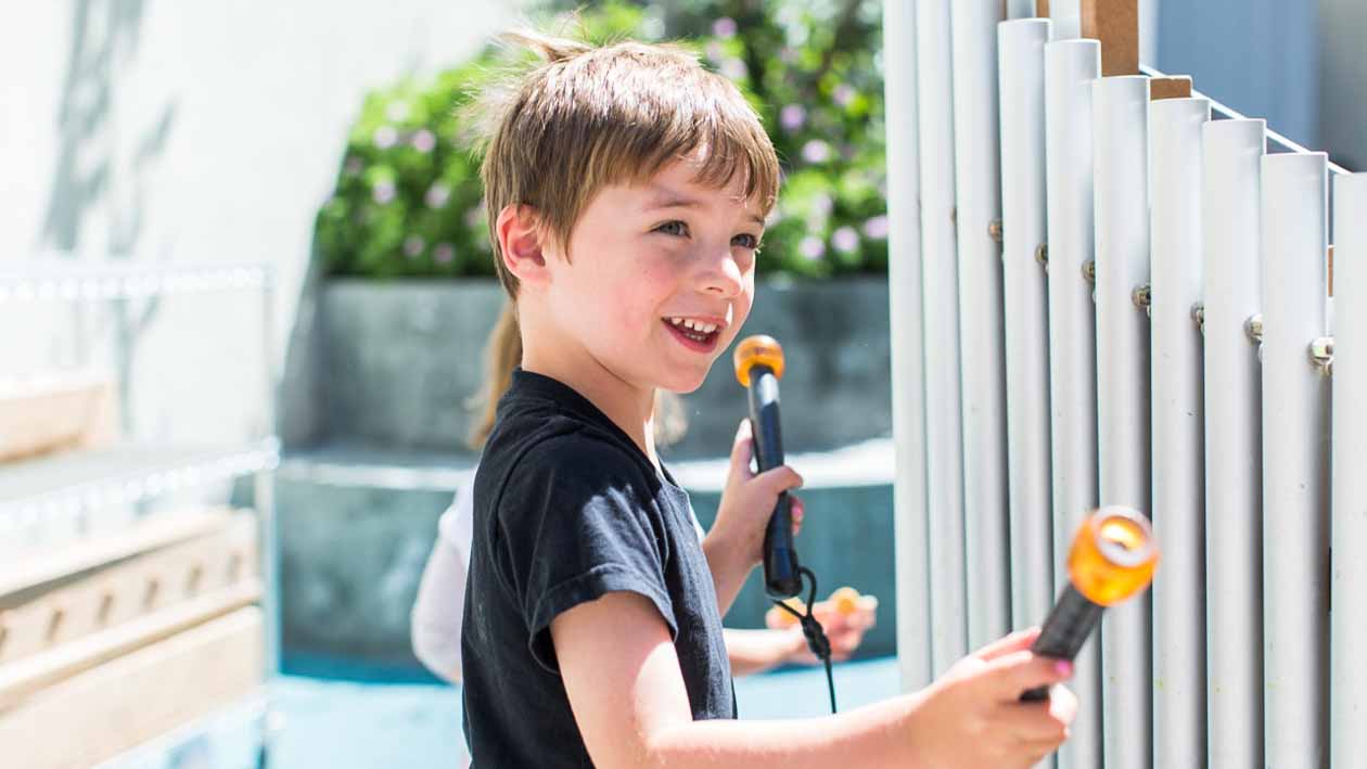 Young boy plays outdoor musical pipes