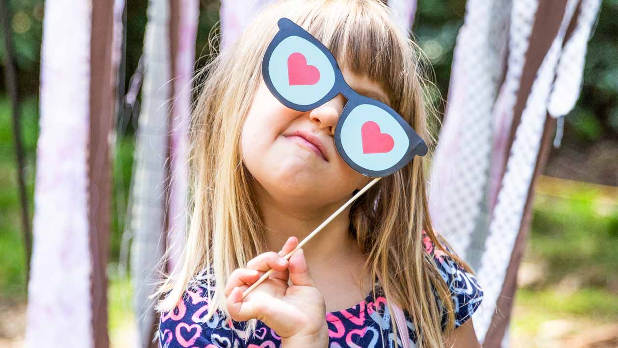 Young girl holds paper glasses with hearts in front of face