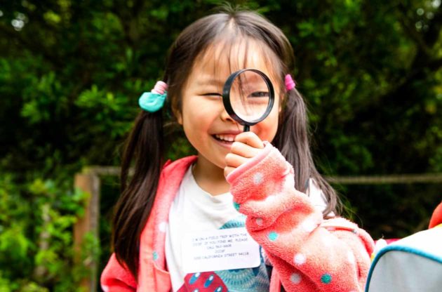 Smiling girl holds magnifying glass in front of face