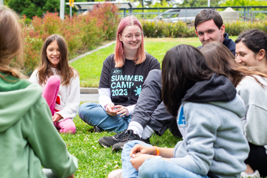 Summer camp counselors play games outside with a group of children.