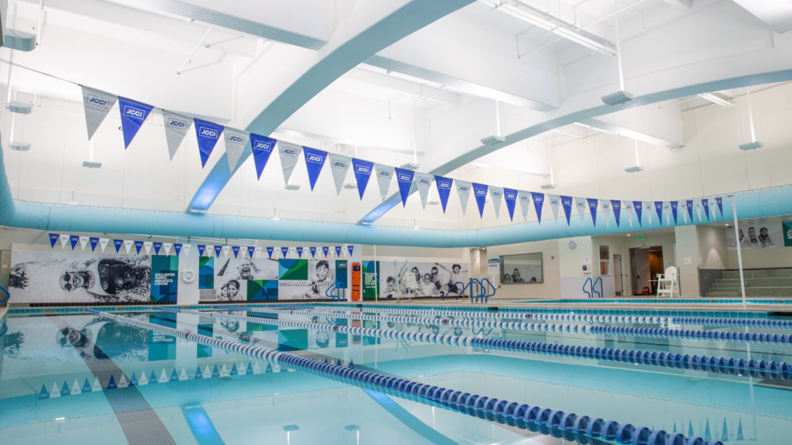 clear blue pool with lane markers and blue and white flags hanging above the pool that say JCCSF.