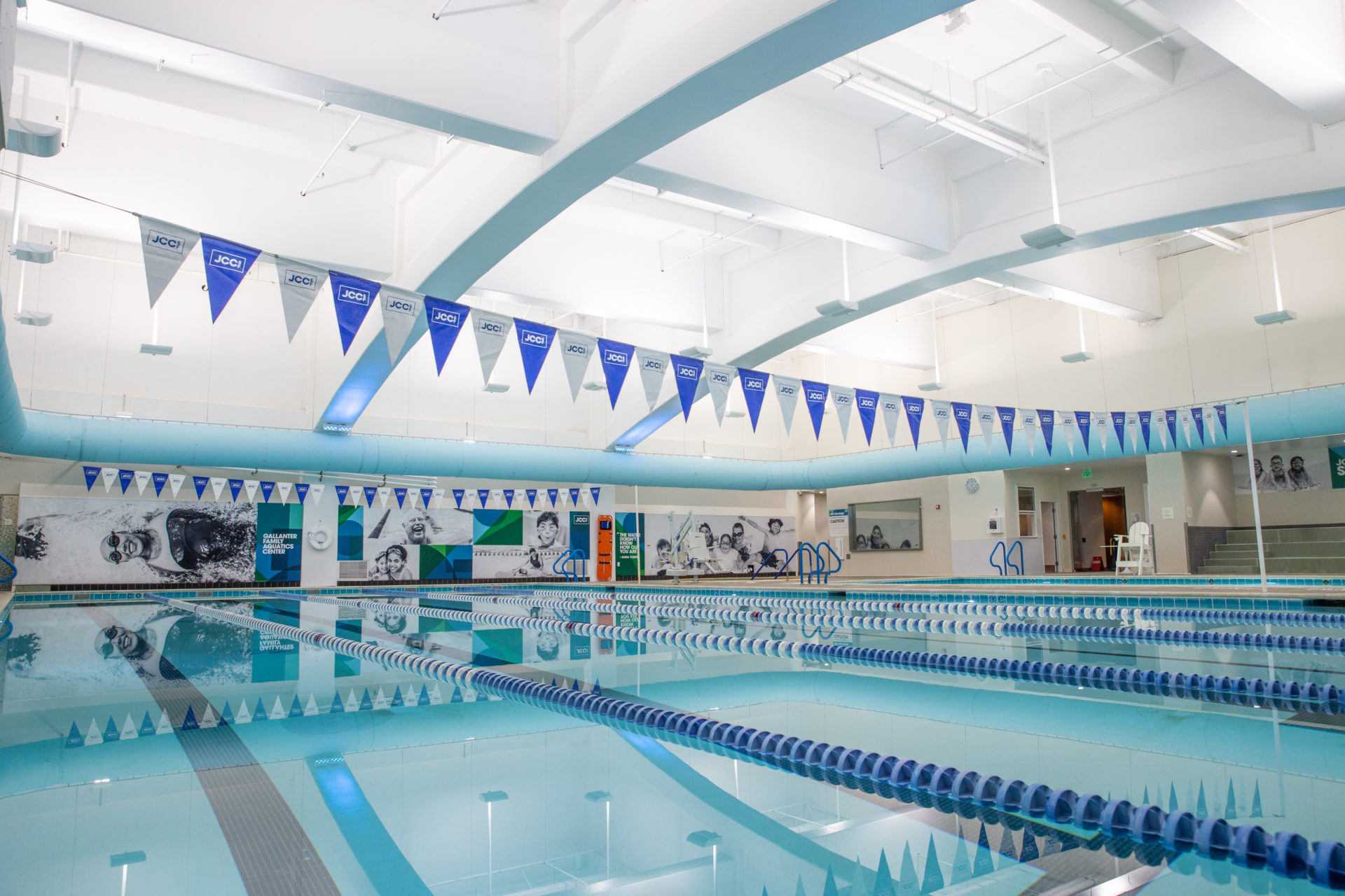 clear blue pool with lane markers and blue and white flags hanging above the pool that say JCCSF.