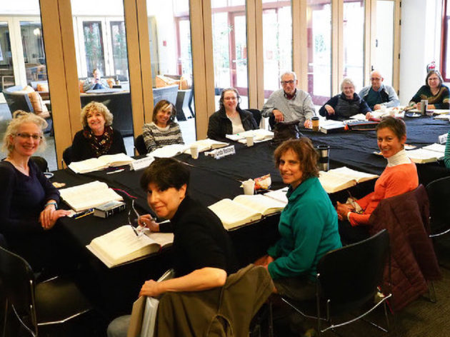 A group sits around a table reading and discussing the Torah.