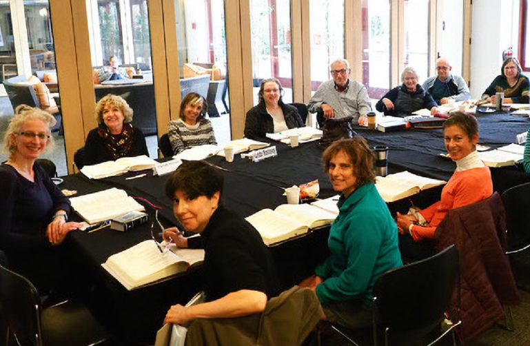 A group sits around a table reading and discussing the Torah.