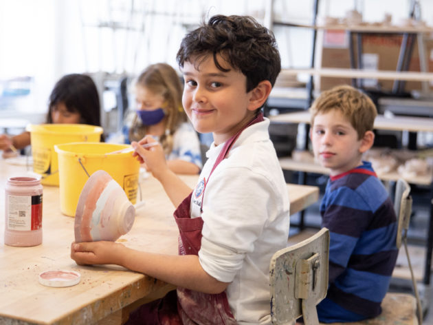 Young boy smiling while glazing a bowl.
