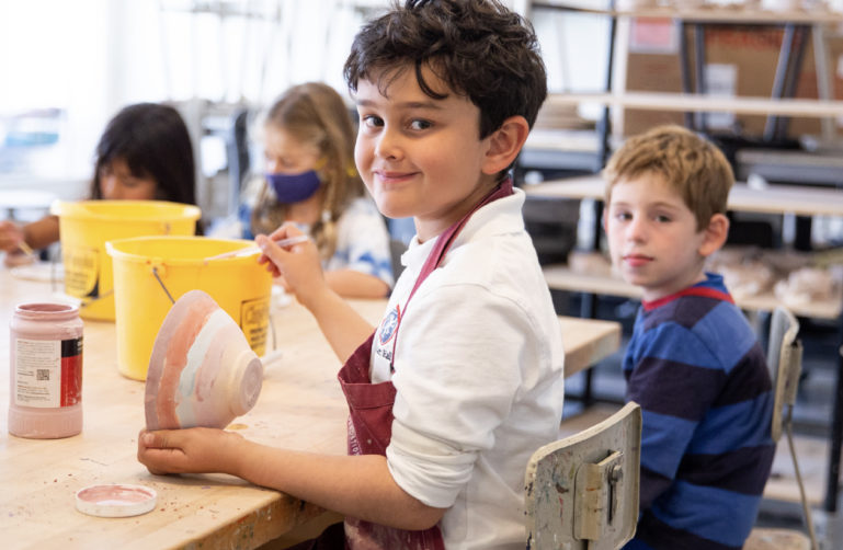 Young boy smiling while glazing a bowl.