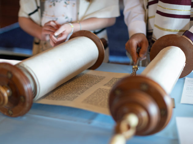 Image of the Torah unrolled on a table being read.
