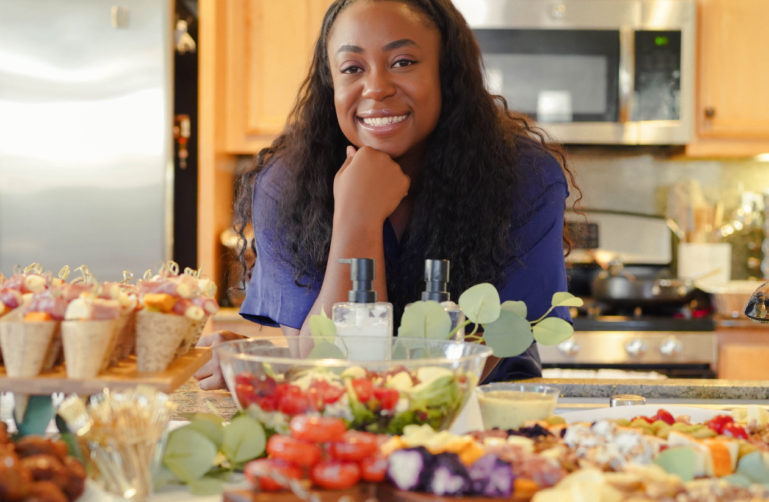 Chef Vee smiling in a kitchen filled with fresh produce.