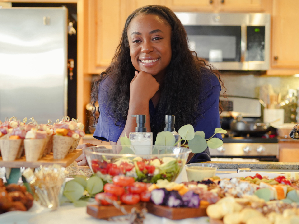 Chef Vee smiling in a kitchen filled with fresh produce.